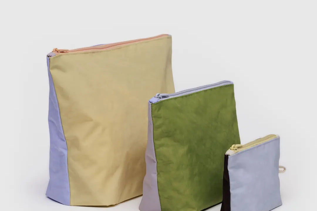 Drei Stoffbeutel in unterschiedlichen Größen sind auf einem schlichten Hintergrund abgebildet. Der größte ist gelb mit einer lavendelfarbenen Seite, der mittlere ist grün und lavendelfarben und der kleinste ist hellblau mit braun.