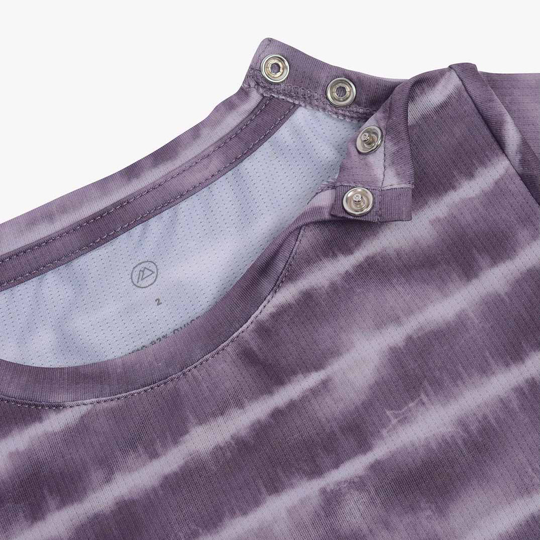 Nahaufnahme eines violetten Hemdkragens mit Batikmuster und zwei Metalldruckknöpfen, teilweise geöffnet. Das Hemd, das an ein Aina Kinder UV-Shirt von Main Design mit UPF 50+ Sonnenschutz erinnert, hat ein weißes Netz-Innenfutter aus nachhaltigem Stoff. Der Hintergrund ist weiß.