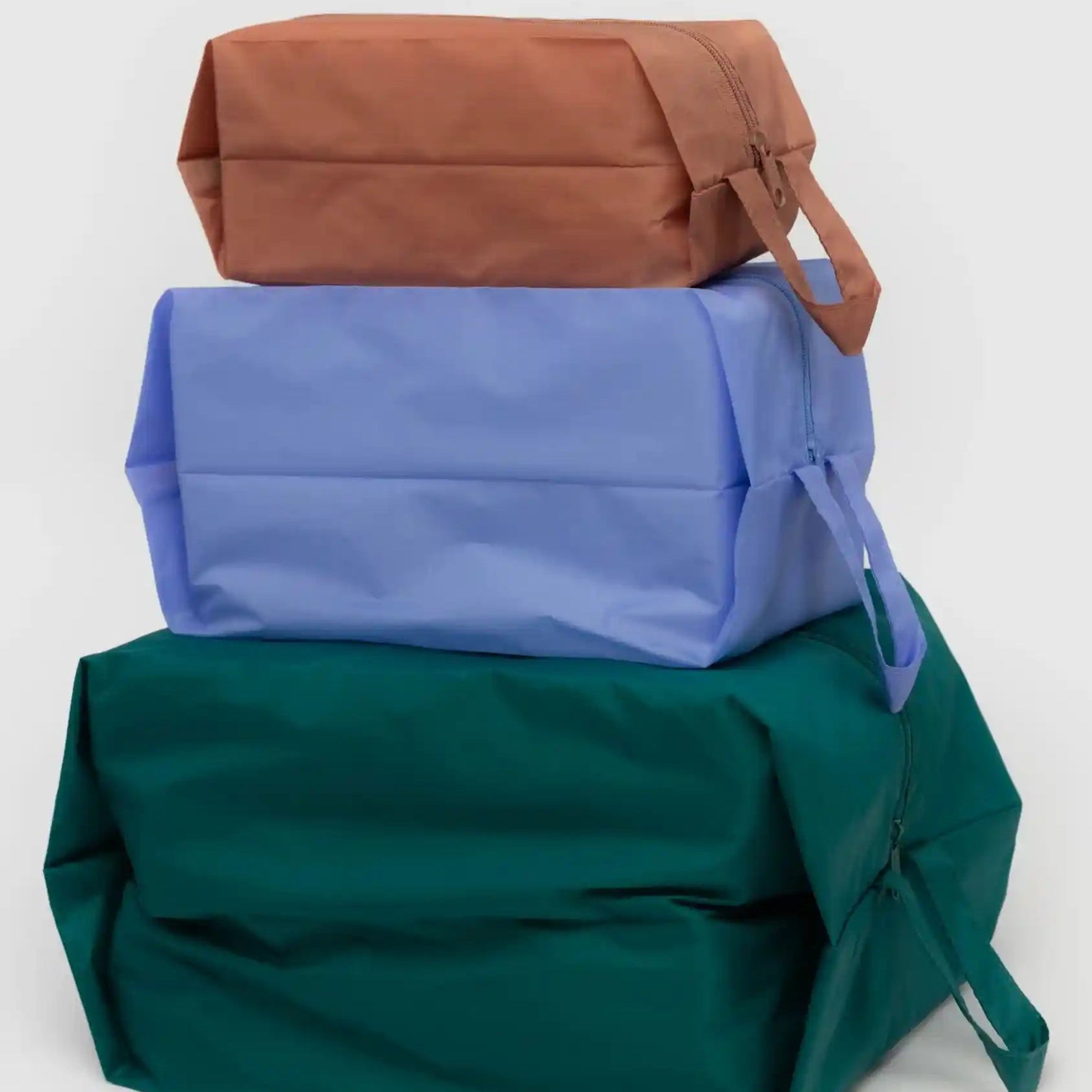 Das BAGGU 3D Zip Set der Marke BAGGU zeigt drei rechteckige Reißverschlusstaschen in Braun, Hellblau und Dunkelgrün mit seitlichem Henkel - ideal als Reise-Organizer.