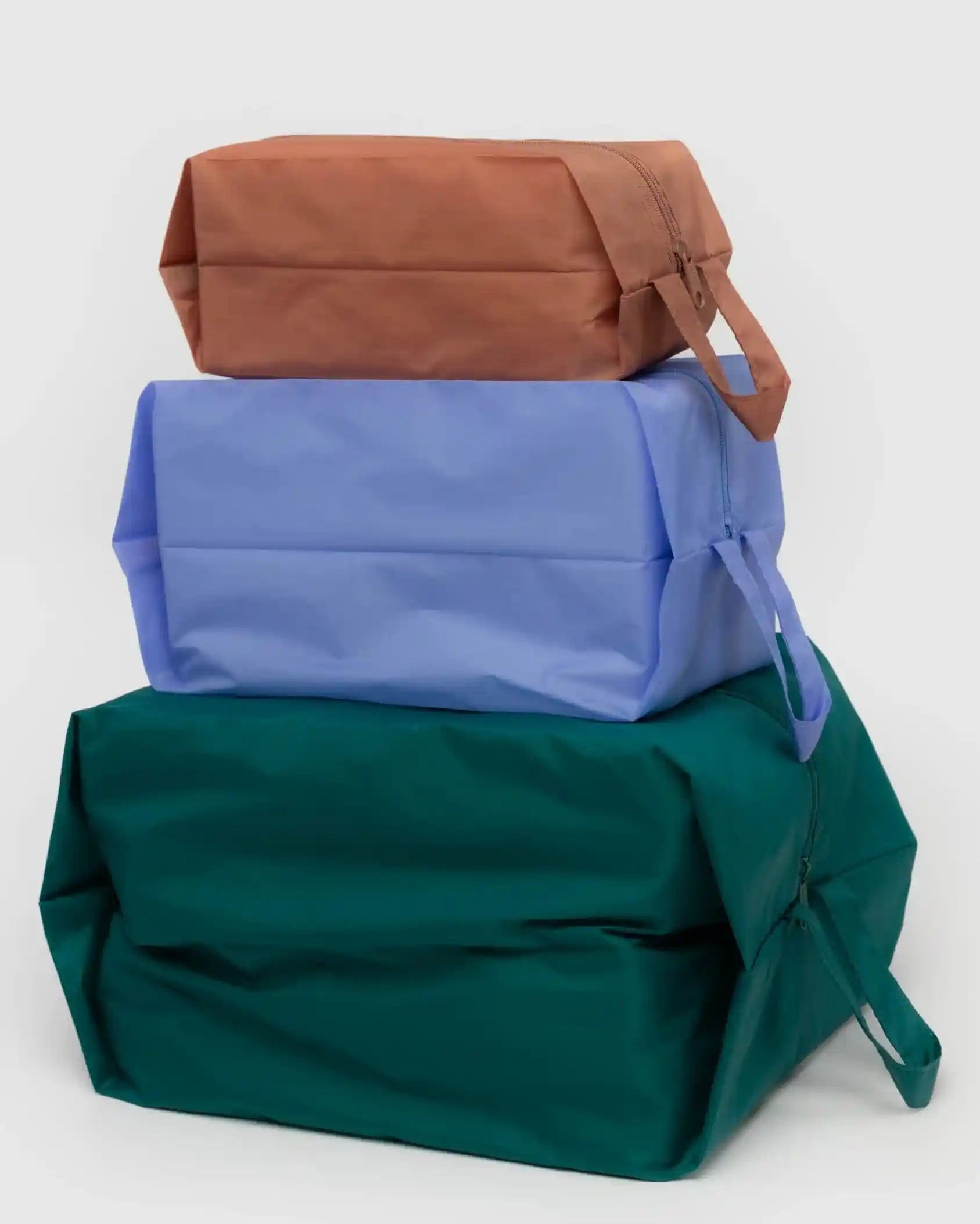 Das BAGGU 3D Zip Set der Marke BAGGU zeigt drei rechteckige Reißverschlusstaschen in Braun, Hellblau und Dunkelgrün mit seitlichem Henkel - ideal als Reise-Organizer.