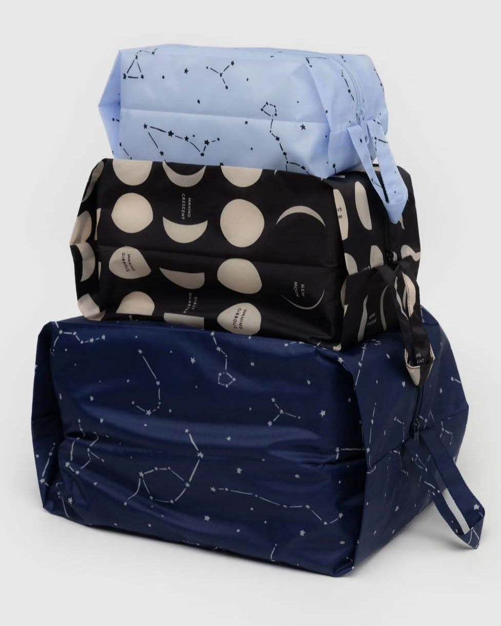 Das BAGGU 3D Zip Set von BAGGU besteht aus drei rechteckigen Beuteln mit Griffen: hellblau mit Sternbildern, schwarz mit Mondphasen und dunkelblau mit Sternbildern - ideal für die Reise.