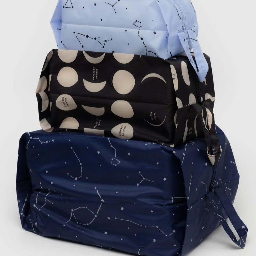 Das BAGGU 3D Zip Set von BAGGU besteht aus drei rechteckigen Beuteln mit Griffen: hellblau mit Sternbildern, schwarz mit Mondphasen und dunkelblau mit Sternbildern - ideal für die Reise.