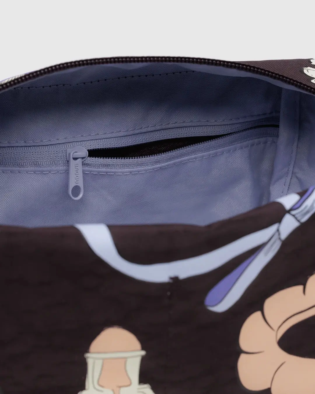 Nahaufnahme eines geöffneten BAGGU Dopp Kit Necessaire von BAGGU, mit einem hellvioletten Innenraum mit einer Reißverschlusstasche und einem Teil einer illustrierten dunklen Außenseite - perfekt als stilvolles Reiseaccessoire.