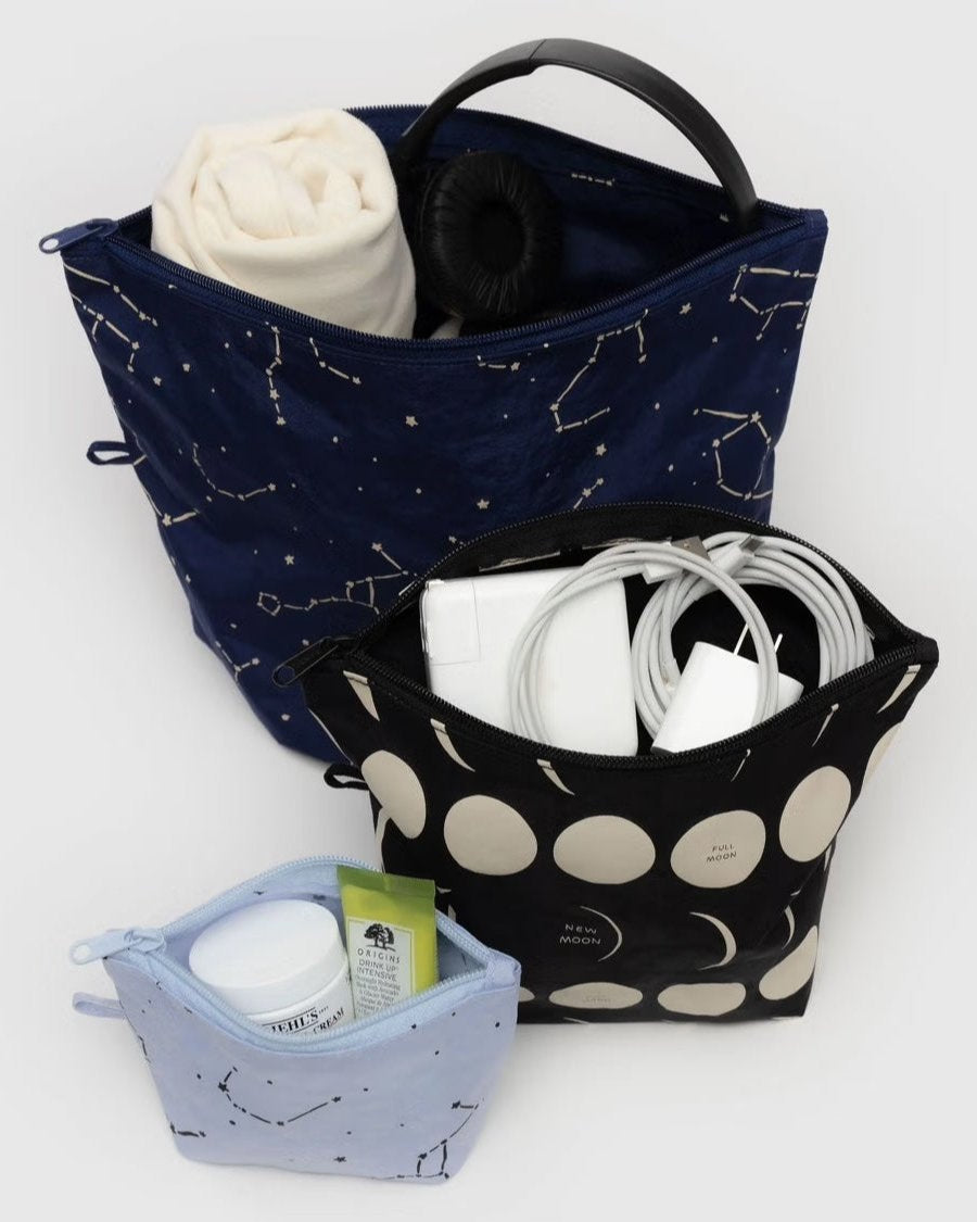 Das BAGGU Go Pouch Set von BAGGU enthält drei Taschen aus recyceltem Nylon: eine große Tasche mit Sternbildaufdruck für Stoff und Kopfhörer, eine mittlere Tasche mit Mondmuster für Kabel und eine kleine Tasche für Glas, Tube und Tupfer.