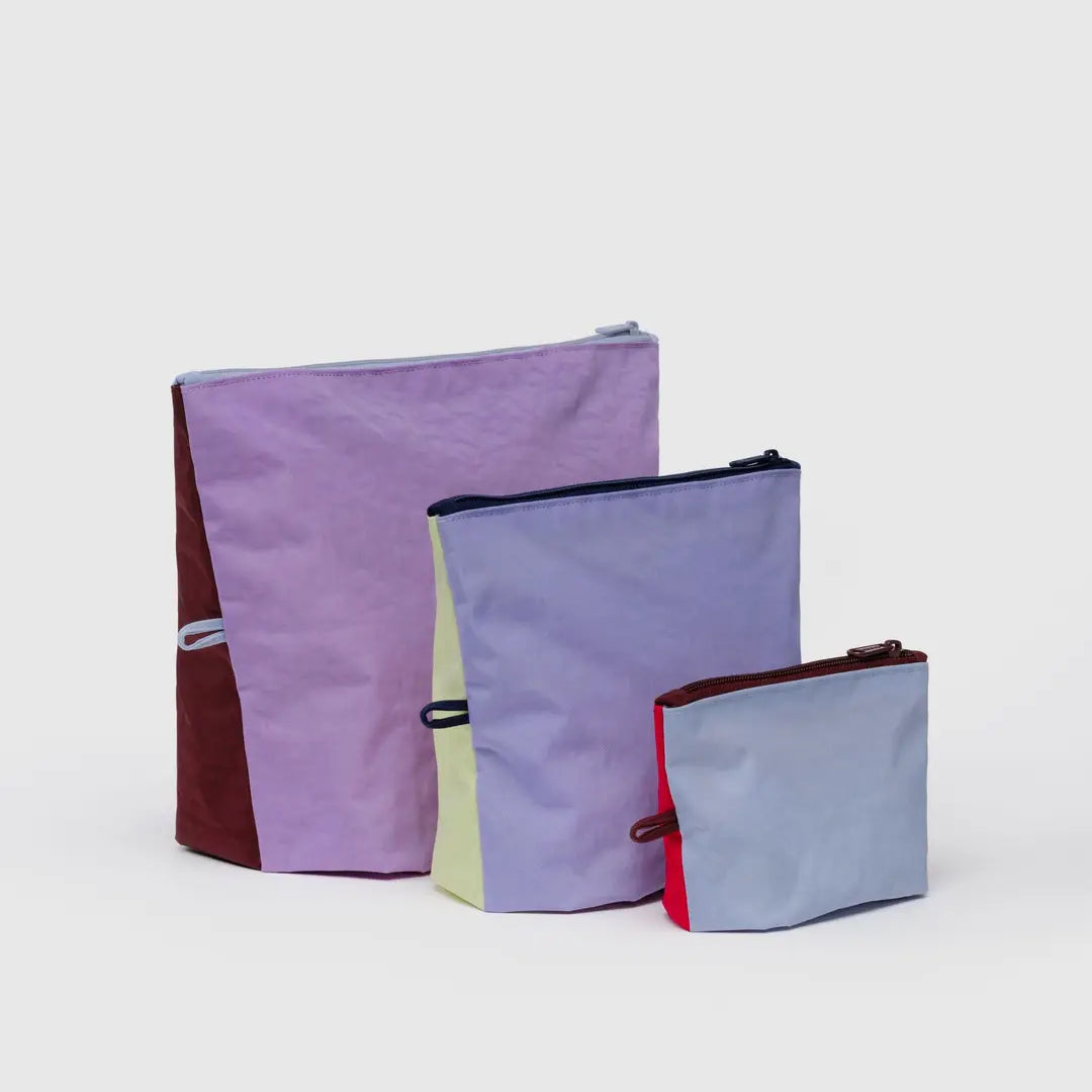 Drei farbige BAGGU Go Pouch Set Allzwecktaschen von BAGGU in verschiedenen Größen sind auf einem unifarbenen Hintergrund abgebildet und zeigen Pastell- und kräftige Farbtöne - Lavendel, Gelb, Braun, Blau und Rot - aus recyceltem Nylon.