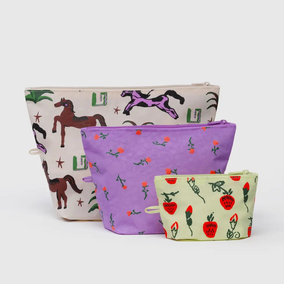 Das BAGGU Go Pouch Set von BAGGU enthält drei Taschen aus recyceltem Nylon: eine große Tasche mit Pferde- und Kaktusmotiven, eine mittlere Tasche mit lila Blumenmuster und eine kleine hellgrüne Tasche mit roten Erdbeeren und grünen Ranken.