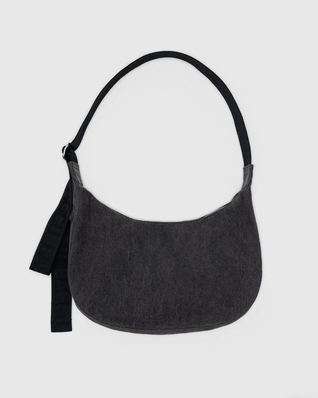 Die BAGGU Medium Denim Crescent Bag von BAGGU ist eine dunkelgraue, halbmondförmige Tasche mit einem breiten schwarzen Riemen und einem schwarzen Stoffanhänger auf der linken Seite. Sie ist aus recycelter Baumwolle gefertigt und auf einem einfarbigen hellgrauen Hintergrund abgebildet.
