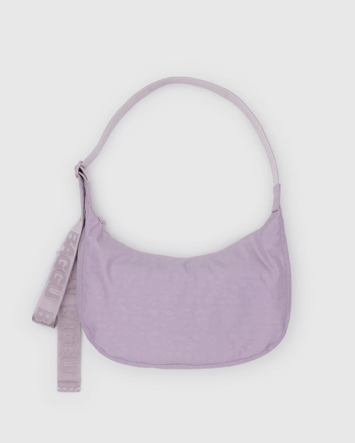 Die BAGGU Medium Nylon Crescent Bag in pastellfarbenem Lavendel hat eine geschwungene Form, einen verstellbaren Riemen und einen passenden abnehmbaren "BAGGU"-Schlüsselanhänger auf der linken Seite, der auf einem hellgrauen Hintergrund abgebildet ist.