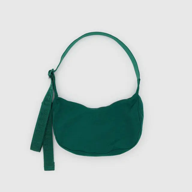 Die BAGGU Small Nylon Crescent Bag von BAGGU ist eine kompakte grüne Umhängetasche mit geschwungener Silhouette, breitem Riemen und Stoffanhänger, hergestellt aus recyceltem Nylon und abgebildet auf einem schlichten hellgrauen Hintergrund.
