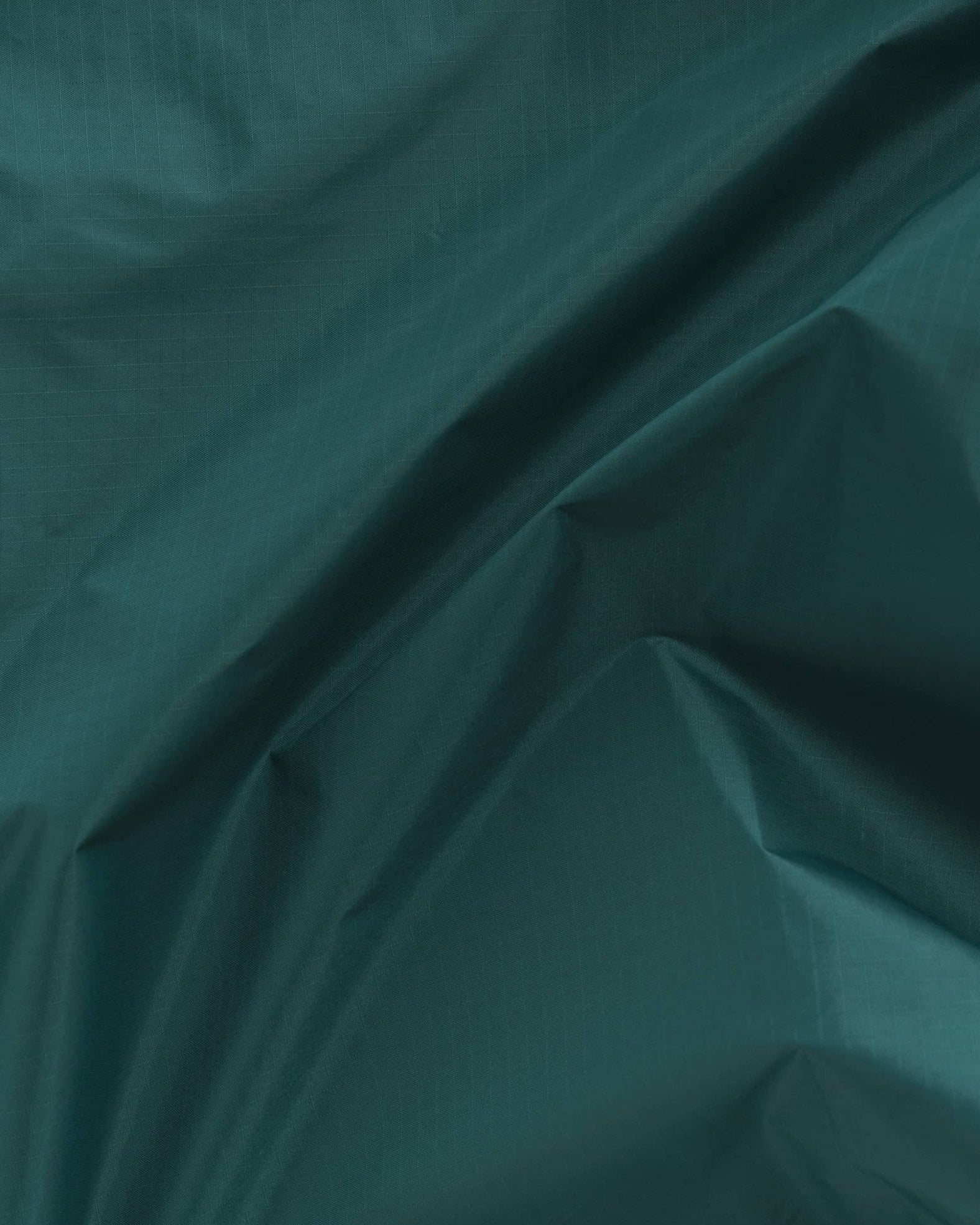 Die zerknitterte und faltige dunkelgrüne Stofftextur mit leichtem Glanz erzeugt ein Muster aus Falten und Schatten, das an das recycelte Ripstop-Nylon erinnert, das in der BAGGU Standard Tragetasche von Main Design verwendet wird.