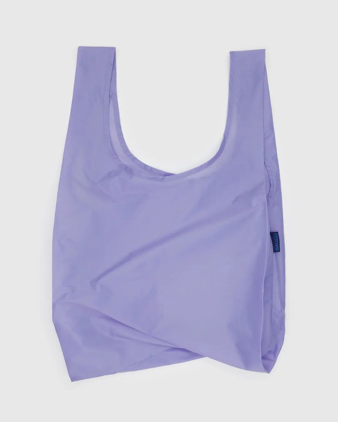 Die BAGGU Standard Tragetasche der Marke BAGGU ist aus recyceltem Ripstop-Nylon in hellem Lila gefertigt, nachhaltig und wiederverwendbar. Sie hat breite Henkel, eine schlichte rechteckige Form und wird flach auf weißem Hintergrund gezeigt.