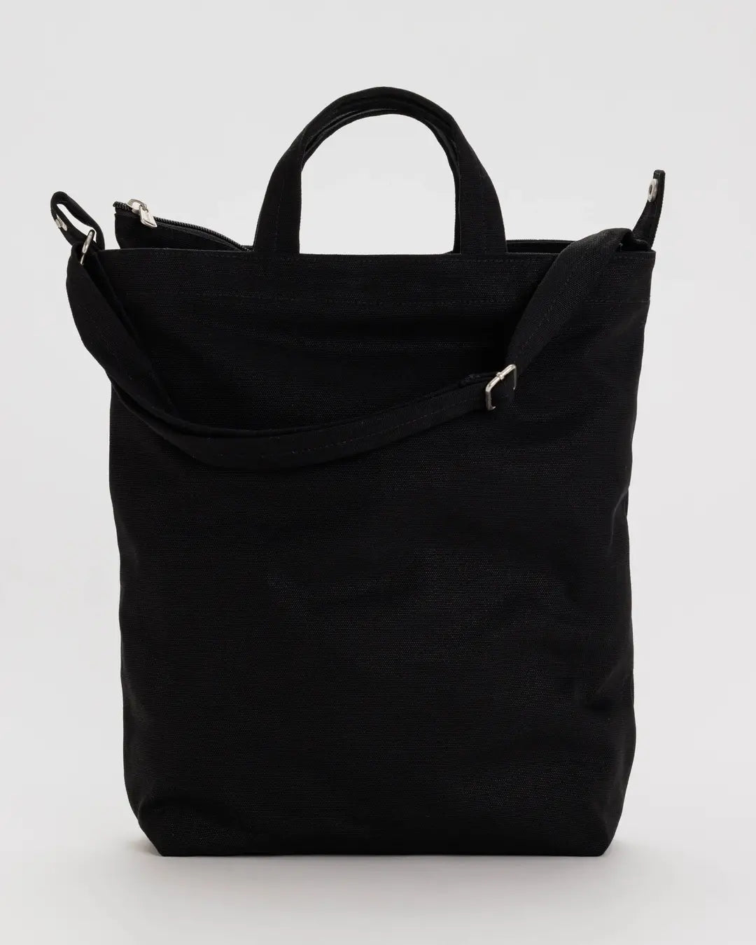 Die BAGGU Zip Duck Bag aus recycelter Baumwolle in Schwarz mit kurzen Henkeln, langem verstellbarem Schulterriemen und Reißverschluss von BAGGU vor hellgrauem Hintergrund.