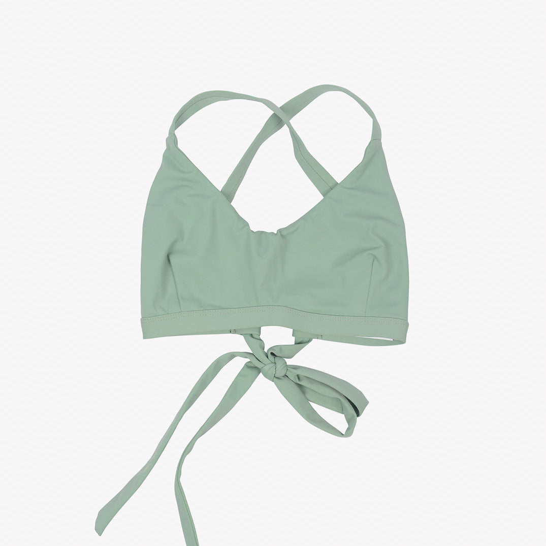Ein hellgrünes Charm Surf Bikini Oberteil von Main Design mit überkreuzten Trägern auf der Rückseite und einem Bindeverschluss vorne. Das Bralette aus umweltfreundlichem Stoff liegt flach auf einem weißen Hintergrund.