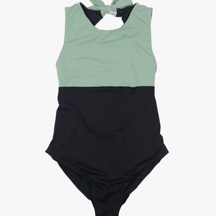 Der Divine Surf Badeanzug von Main Design ist ein ärmelloser einteiliger Badeanzug mit hohem Halsausschnitt und Neckholder-Bindeband auf der Rückseite. Der obere Teil ist hellgrün und der untere Teil schwarz. Er besteht aus umweltfreundlichem Stoff und bietet LSF 50+-Schutz, ist weich und dehnbar und auf Komfort und Stil ausgelegt.