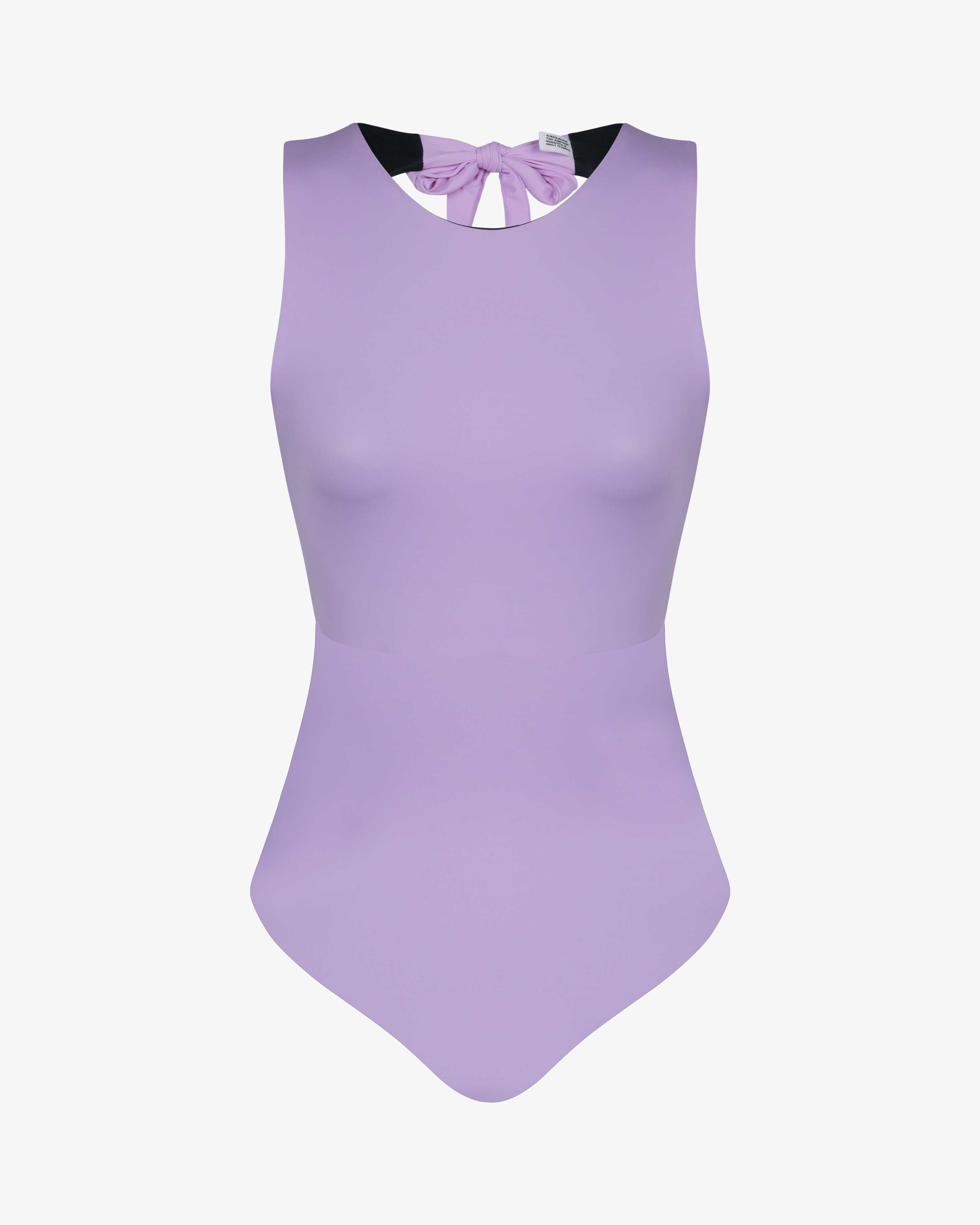 Der Divine Surf Badeanzug von Main Design ist ein ärmelloser, hellvioletter Badeanzug mit hohem Ausschnitt und einer Schleife am Rücken. Er ist aus recycelten Materialien gefertigt und wird auf einem schlichten weißen Hintergrund gezeigt.