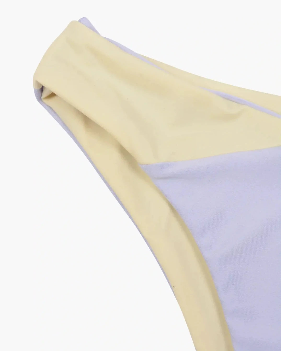 Nahaufnahme einer Flair-Bikinihose aus der Cali Coast Collection von Main Design, die einen blassen Gelb- und Lavendel-Colorblock-Stil auf glattem, leicht dehnbarem Stoff vor einem schlichten weißen Hintergrund zeigt.