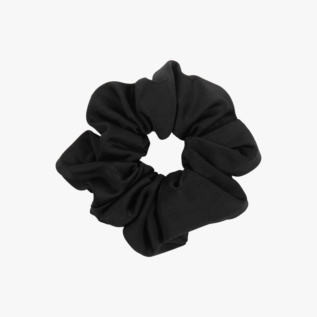 Ein einfarbiges Haargummi aus schwarzem Stoff von Main Design ist auf einem schlichten weißen Hintergrund abgebildet. Das Haargummi ist kreisförmig gerafft, wobei sich der gerüschte Stoff nach außen erstreckt, was das Engagement für nachhaltige Modeentscheidungen unterstreicht.