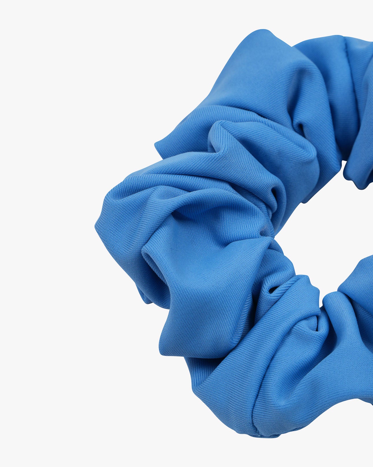 Eine Nahaufnahme des einfarbigen Haargummis von Main Design, einem blauen Stoff-Scrunchie mit weicher, geraffter Textur aus Stoffresten – eine nachhaltige Wahl für Ihre Haargummi-Sammlung, vor weißem Hintergrund.