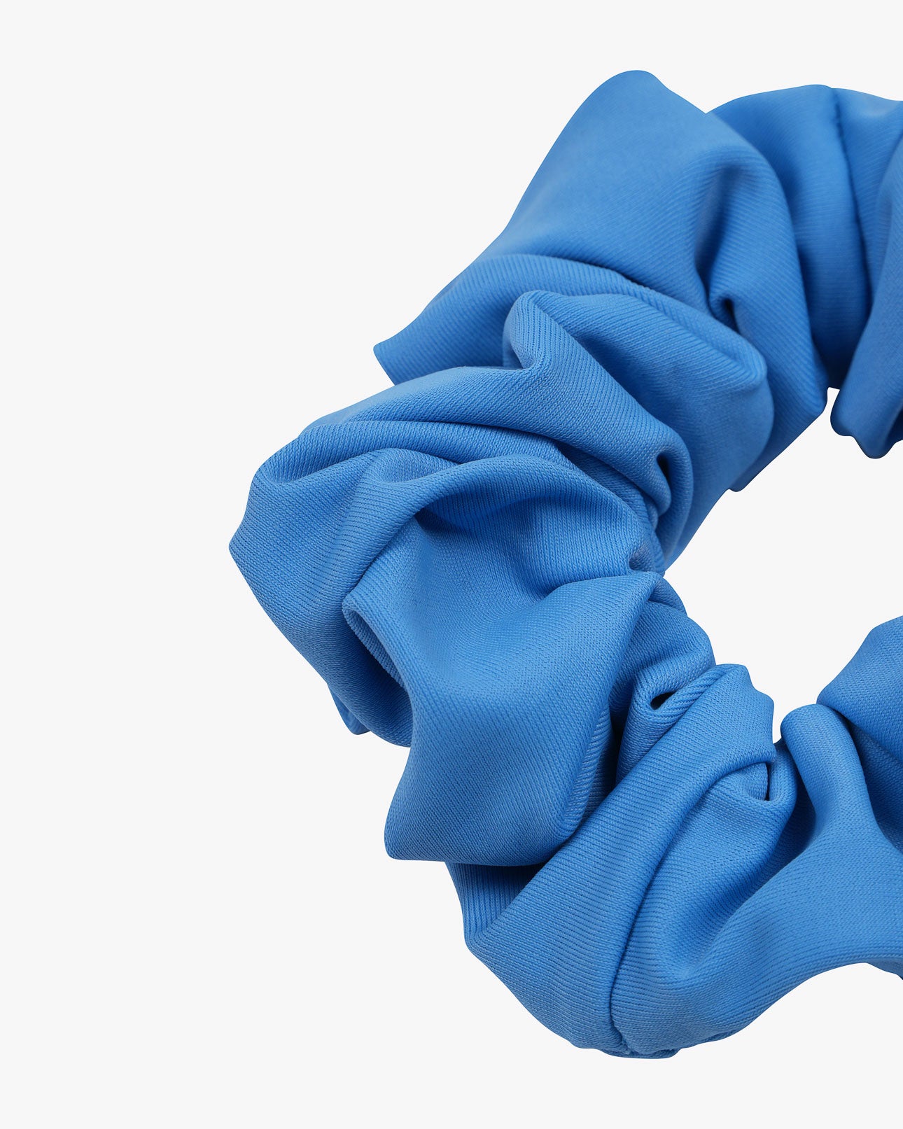 Eine Nahaufnahme des einfarbigen Haargummis von Main Design, einem blauen Stoff-Scrunchie mit weicher, geraffter Textur aus Stoffresten – eine nachhaltige Wahl für Ihre Haargummi-Sammlung, vor weißem Hintergrund.