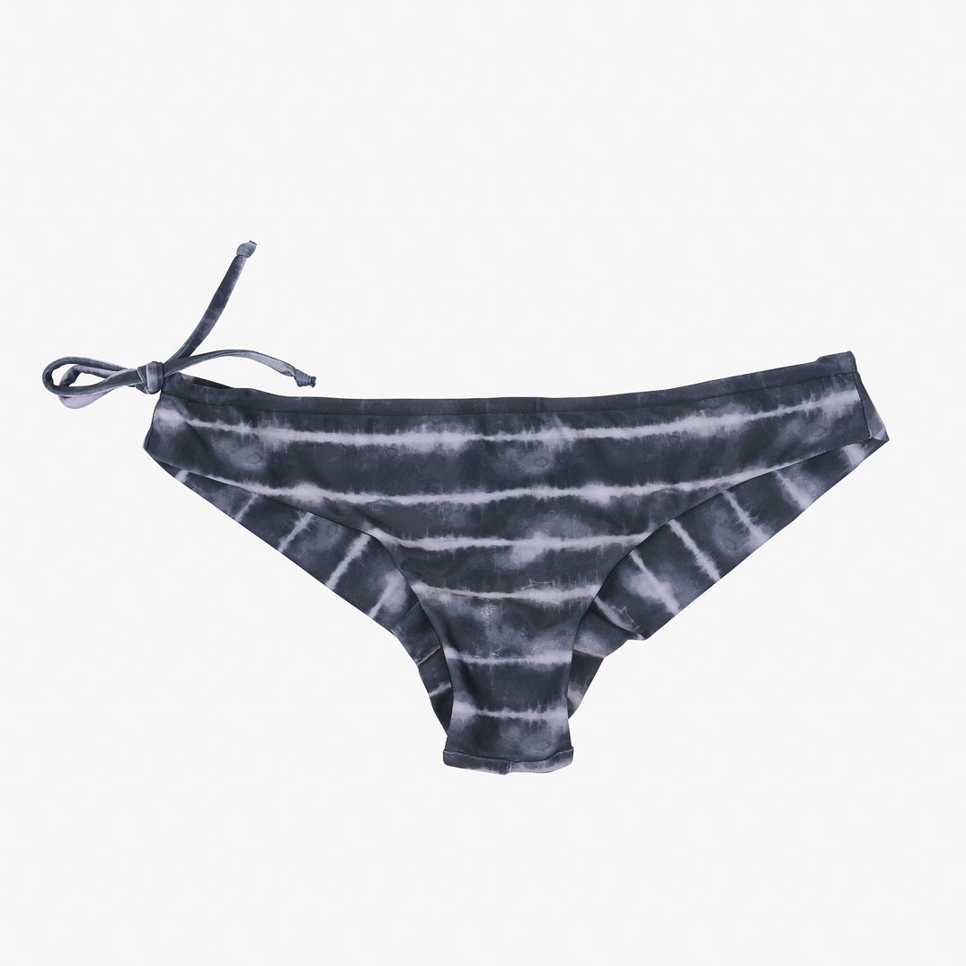 Ein Paar Bikinihöschen für Damen mit einem Batikmuster in Grau- und Schwarztönen. Die **Keira Surf Bikini Hose** von **Main Design**, inspiriert von einer Surf-Bikinihose, verfügt über eine seitliche Schleife auf der linken Seite für eine verstellbare Passform. Der Hintergrund ist schlicht weiß.