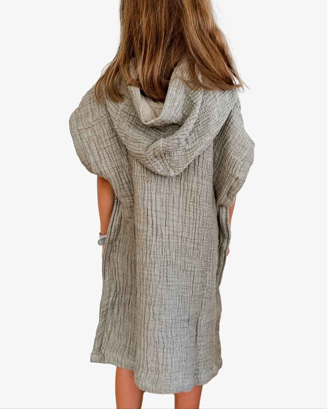 Ein Kind mit langen braunen Haaren steht mit dem Rücken zur Kamera, eingehüllt in den strukturierten grauen Kinder Badeponcho Flow von Main Design aus OEKO-TEX zertifizierter Baumwolle, vor einem schlichten weißen Hintergrund, der seine Eleganz unterstreicht.
