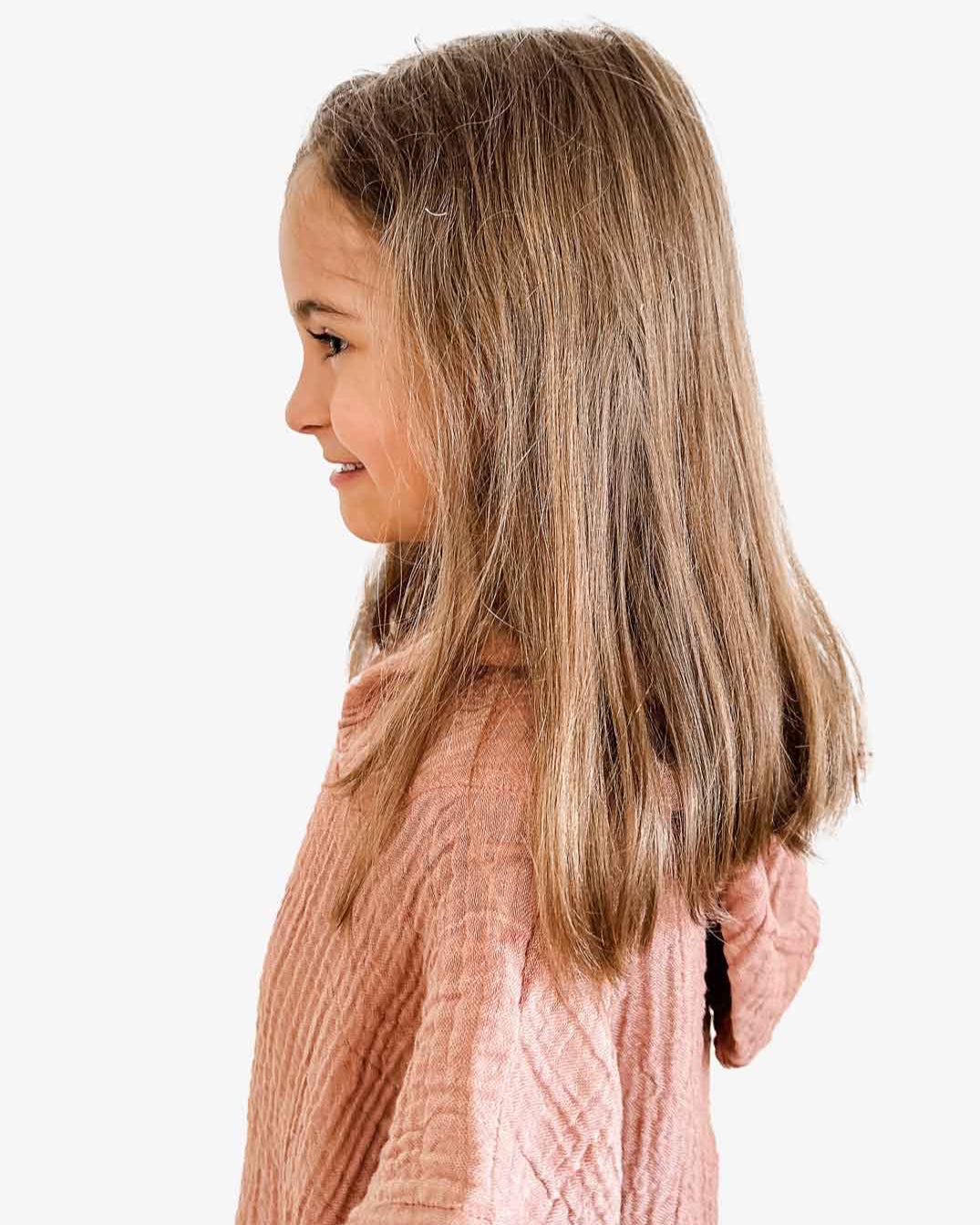 Ein junges Mädchen mit langen braunen Haaren, das den rosa strukturierten Kinder Badeponcho Flow von Main Design aus OEKO-TEX zertifizierter Baumwolle trägt, blickt vor einem weißen Hintergrund nach links.