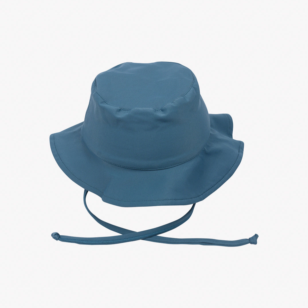 Ein blauer Main Design Kinder-Sonnenhut ist auf einem schlichten weißen Hintergrund abgebildet. Der Hut aus umweltfreundlichem Stoff hat eine nach unten geneigte Krempe und einen verstellbaren Kinnriemen für mehr Sicherheit. Außerdem bietet er Sonnenschutz UPF 50+ für optimalen Sonnenschutz.