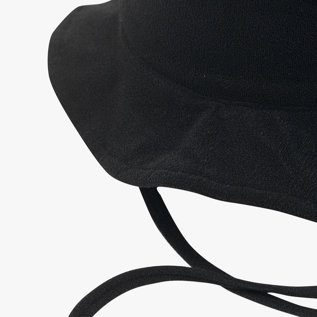 Eine Nahaufnahme eines schwarzen Kinder-Sonnenhuts mit breiter Krempe und zwei herabhängenden Kinnriemen. Der Hut aus umweltfreundlichem Stoff hat ein einfaches, schmuckloses Design und steht vor einem schlichten weißen Hintergrund.