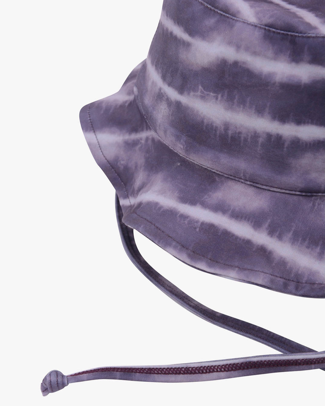 Eine Nahaufnahme eines Batik-Kinder-Sonnenhuts von Main Design in den Farben Schwarz, Dunkelgrau und Lila. Der Hut verfügt über einen verstellbaren Kinnriemen und eine breite Krempe. Der aus umweltfreundlichem Stoff gefertigte Stoff hat ein welliges, gestreiftes Muster für einen unverwechselbaren und lebendigen Look. Der Hintergrund ist schlicht weiß.