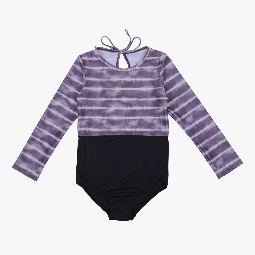 Ein langärmliger Kinderbadeanzug mit einem lila-weißen Batikmuster auf der Oberseite und einem Schlüsselloch-Krawattenverschluss im Nacken. Der untere Teil des Laila Mädchen Badeanzugs von Main Design ist einfarbig schwarz und bietet ein zweifarbiges Design. Dieser schnell trocknende Badeanzug bietet außerdem Sonnenschutz mit LSF 50+.