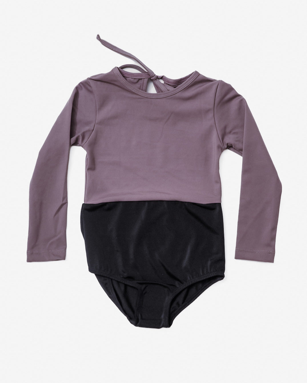 Der Laila Mädchen Badeanzug von Main Design ist ein langarmiger, zweifarbiger Leotard mit einem malvenfarbenen Oberteil mit LSF 50+ Sonnenschutz und einem schwarzen Unterteil. Er verfügt über einen Bindeverschluss auf der Rückseite und ist wunderschön auf weißem Hintergrund dargestellt, ideal für alle, die stilvolle und dennoch schützende Badebekleidung suchen.