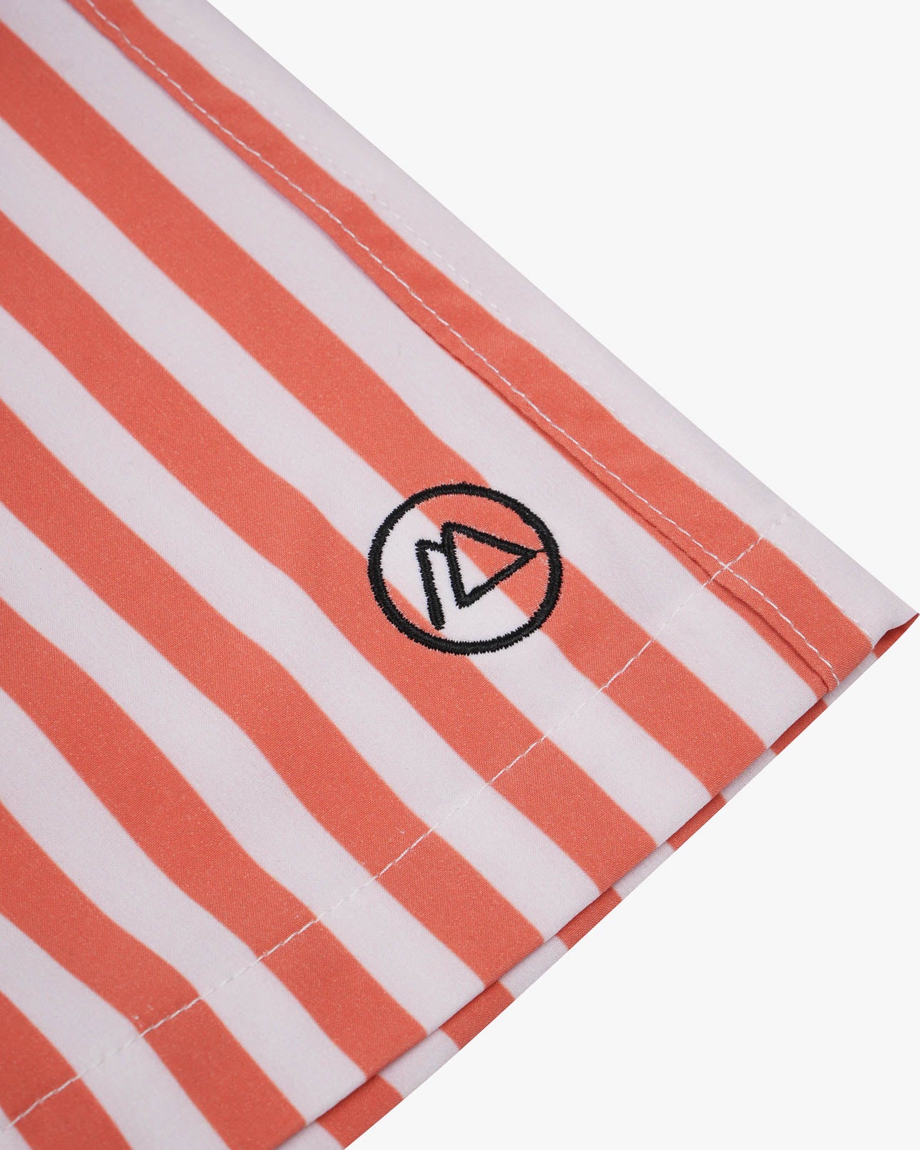 Nahaufnahme eines Stoffes mit weißen und orangefarbenen Längsstreifen aus 4-Wege-Stretch für mehr Flexibilität. Ein kleines, kreisförmiges Logo mit einem stilisierten „A“ ist aufgestickt. Perfekt geeignet für die Lean Boardshorts für Jungen von Main Design, ist der Saum an der Unterkante sichtbar.