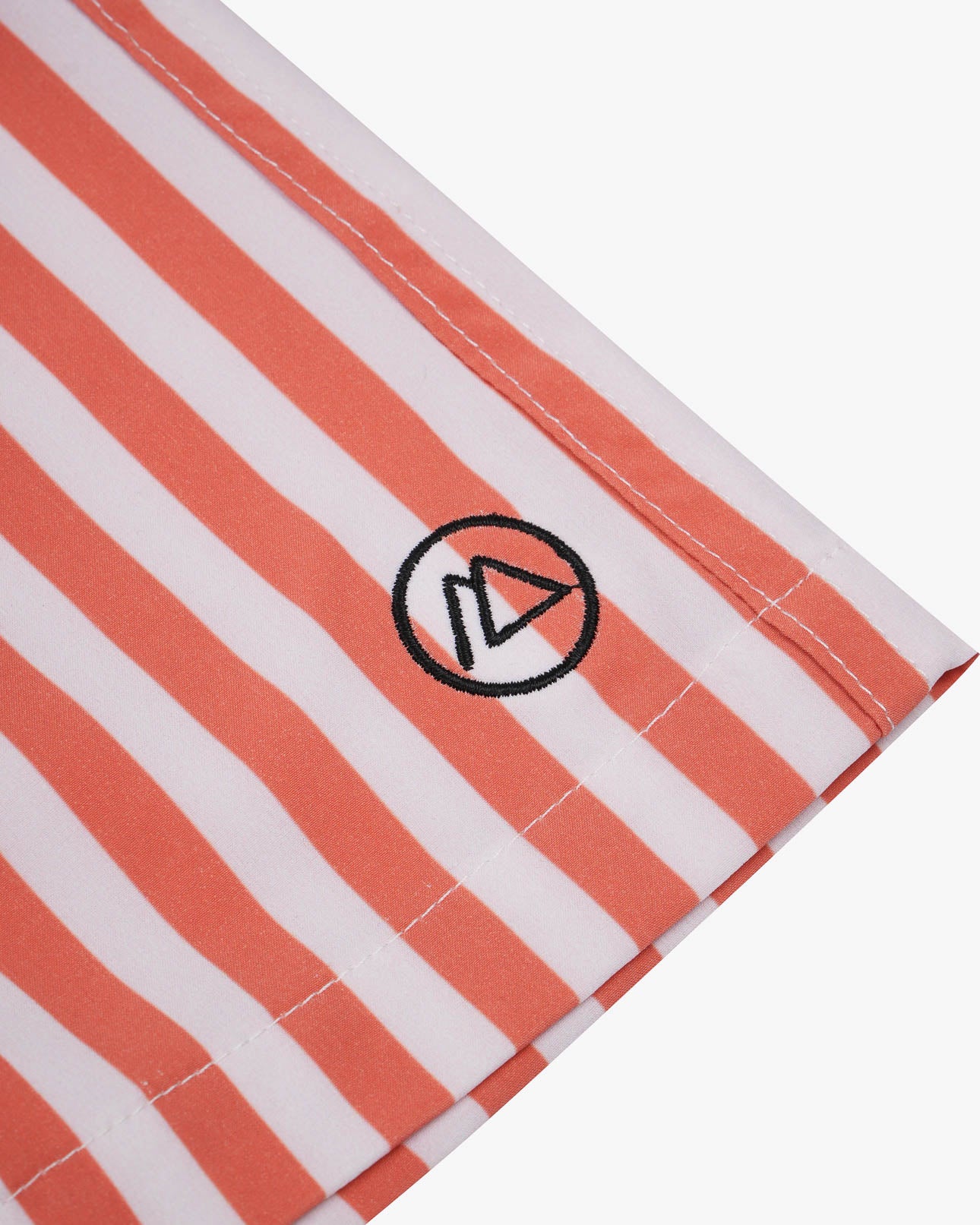 Nahaufnahme eines Stoffes mit weißen und orangefarbenen Längsstreifen aus 4-Wege-Stretch für mehr Flexibilität. Ein kleines, kreisförmiges Logo mit einem stilisierten „A“ ist aufgestickt. Perfekt geeignet für die Lean Boardshorts für Jungen von Main Design, ist der Saum an der Unterkante sichtbar.