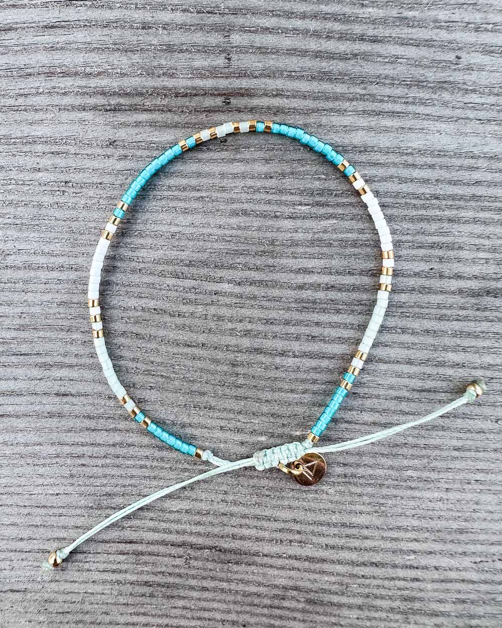 Das Mama und Mini Armband Wave von Main Design ist ein handgefertigtes, nachhaltiges Schmuckstück mit türkis, weißen und goldenen Perlen, verstellbaren Enden und kleinem goldenen Herzanhänger - perfekt als stilvolles Set für Groß und Klein.