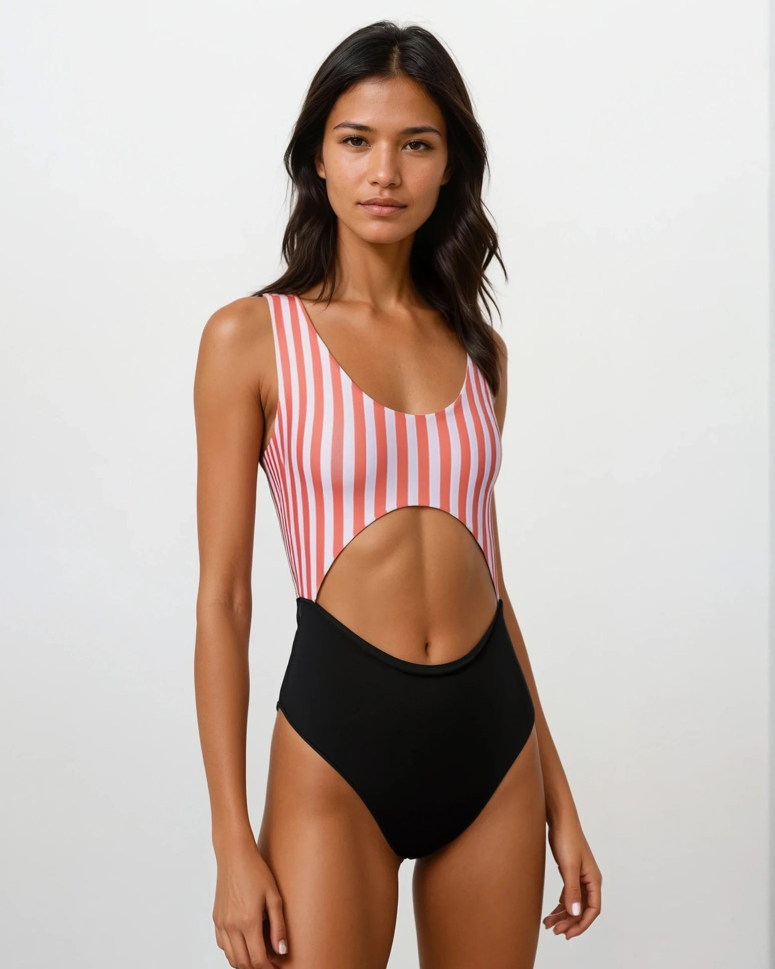 Eine Frau präsentiert vor einem schlichten hellen Hintergrund den Main Design Nova Badeanzug, einen einteiligen Badeanzug mit roten und weißen Streifen oben, einfarbig schwarz unten und einem großen Ausschnitt in der Taille aus recycelten Materialien.
