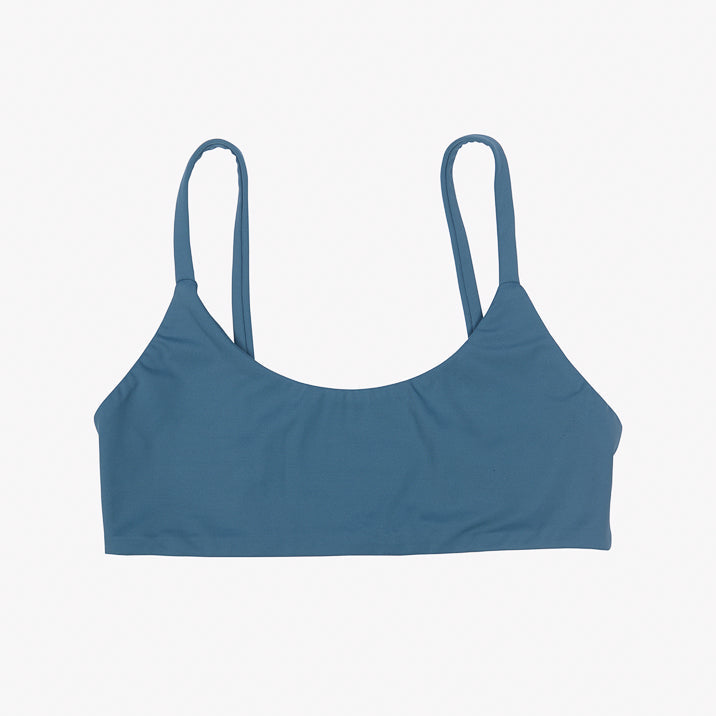 Das Sassy Bikini-Top von Main Design ist ein blaues Bralette mit zwei dünnen Trägern aus recycelten Materialien. Sein glatter, taillierter Stoff bietet einen nahtlosen Schnitt für ultimativen Komfort und ein schlichtes Design, das zu lässiger Kleidung passt. Der schlichte weiße Hintergrund unterstreicht seine lebendige Farbe und Form.