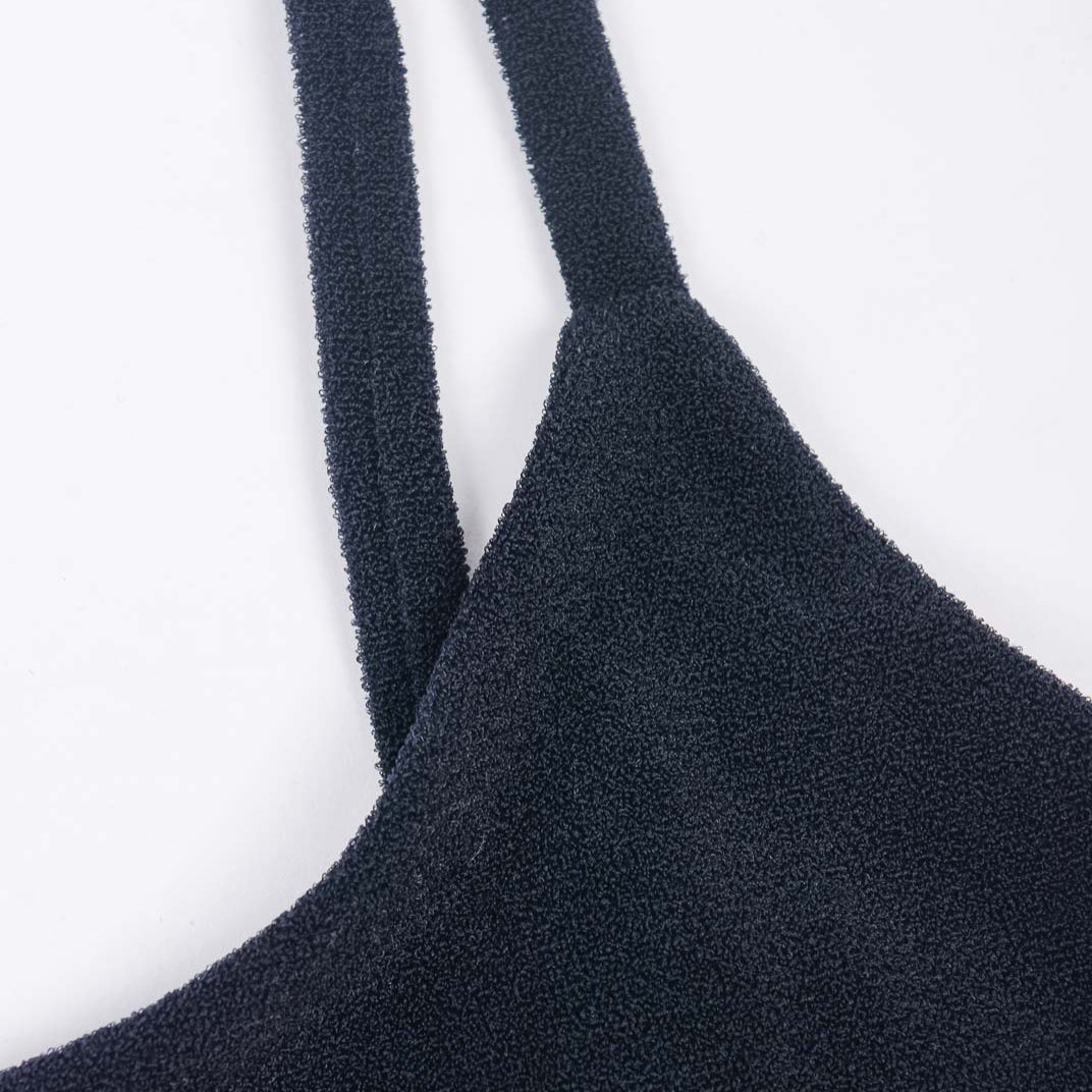 Nahaufnahme des Sassy Bikini-Tops von Main Design aus strukturiertem schwarzem Recyclingstoff mit dünnen Trägern vor weißem Hintergrund. Die raue, taktile Oberfläche des Kleidungsstücks verkörpert mühelos den Stil eines Sassy Bikini-Tops.