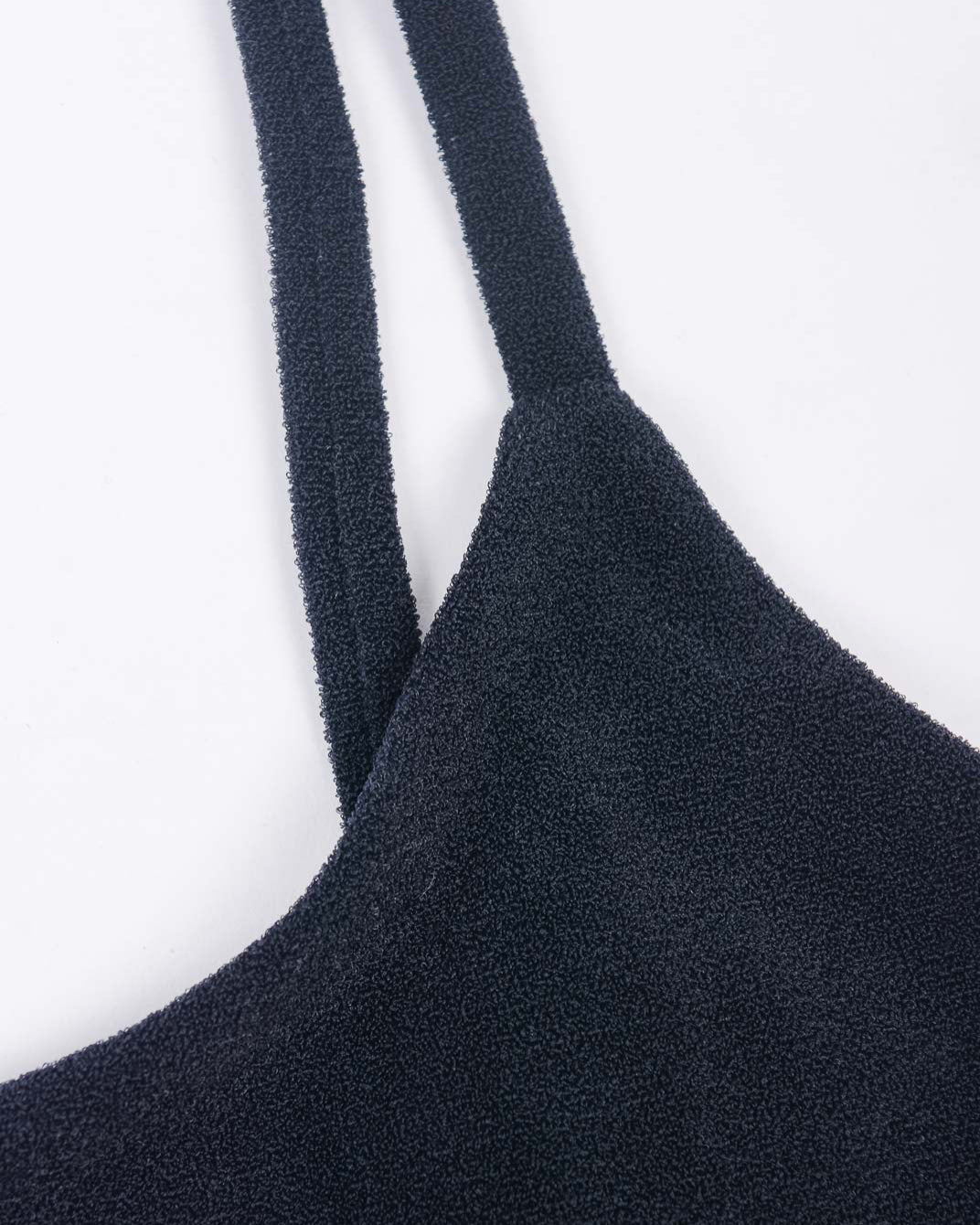 Nahaufnahme des Sassy Bikini-Tops von Main Design aus strukturiertem schwarzem Recyclingstoff mit dünnen Trägern vor weißem Hintergrund. Die raue, taktile Oberfläche des Kleidungsstücks verkörpert mühelos den Stil eines Sassy Bikini-Tops.