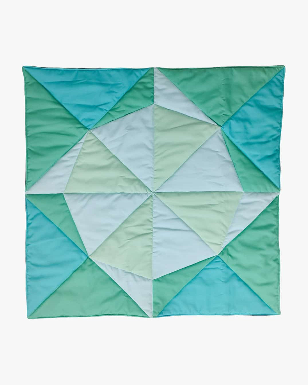 Eine lebendige, handgefertigte Spielmatte und Krabbeldecke Boot von Main Design zeigt ein geometrisches Muster mit unterschiedlichen Grün-, Türkis- und hellblauen Dreiecken auf weißem Hintergrund. Ideal als schicke Krabbelmatte für Ihren Kleinen.