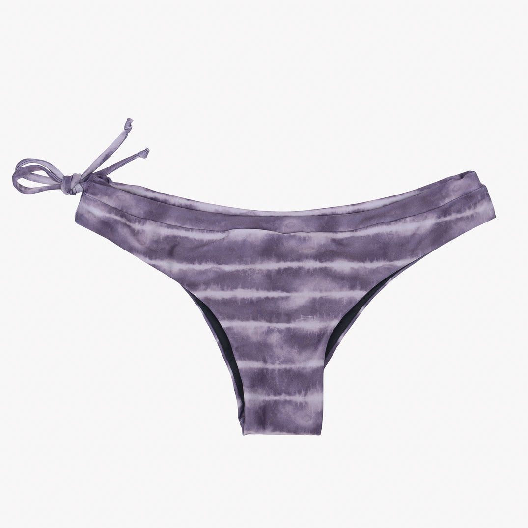 Ein Paar lila Batik-Blush-Surf-Bikinihosen von Main Design mit seitlichem Bindedetail auf der linken Seite. Der Stoff weist horizontale Streifen in verschiedenen Lilatönen auf, die ihm ein dezent gestreiftes Aussehen verleihen. Diese Bikinihose ist aus umweltfreundlichem Stoff gefertigt und hat eine niedrige Leibhöhe.