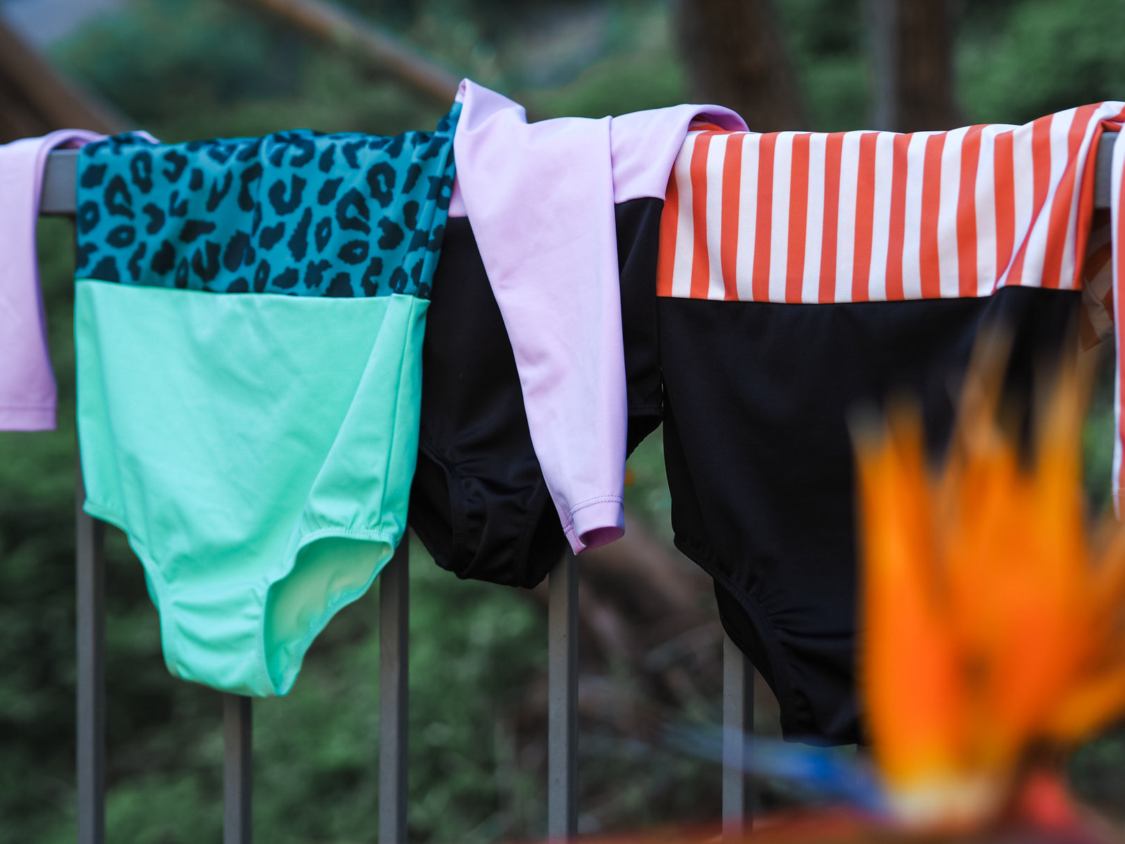 Ein Kind mit nassen Haaren sitzt am Beckenrand und trägt einen zweifarbigen Badeanzug mit Rüschenträgern. Es schaut weg und genießt die Sonne. Der Beckenrand ist aus Stein, im Hintergrund führen Stufen aus dem Becken.