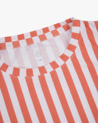 Nahaufnahme eines Main Design Aina Kinder UV-Surfshirts mit vertikalen orangefarbenen Streifen auf weißem Hintergrund. Das schnelltrocknende Shirt mit Rundhalsausschnitt und Größenangabe „5/6“ bietet LSF 50+ für sicheren Sonnenschutz.