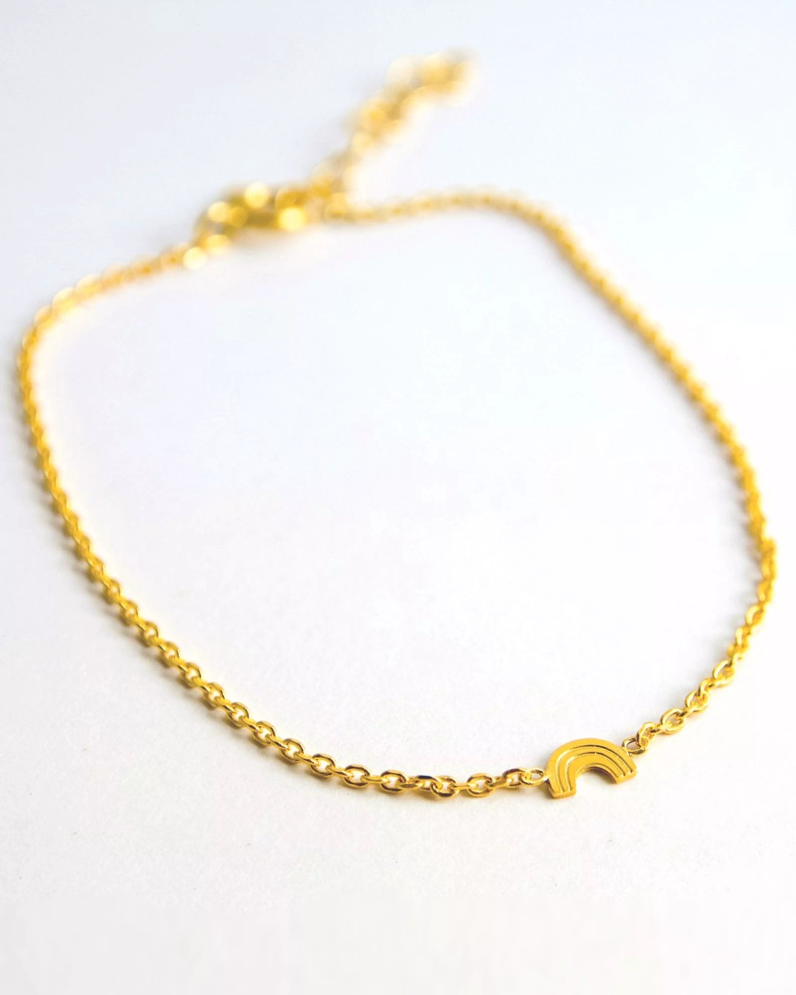 Das Armband von Adorabili ist ein zartes, handgefertigtes Schmuckstück aus 24K vergoldetem Feingold mit einem kleinen Regenbogen-Charm in der Mitte - perfekt für Kinder und präsentiert auf weißem Hintergrund.