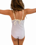 Ein junges Mädchen mit langen braunen Haaren steht mit dem Rücken zur Kamera und streckt die Arme aus. Sie trägt einen Ava Mädchen Badeanzug von Main Design, der am Rücken gebunden wird und verstellbare Träger hat. Der Hintergrund ist schlicht weiß.