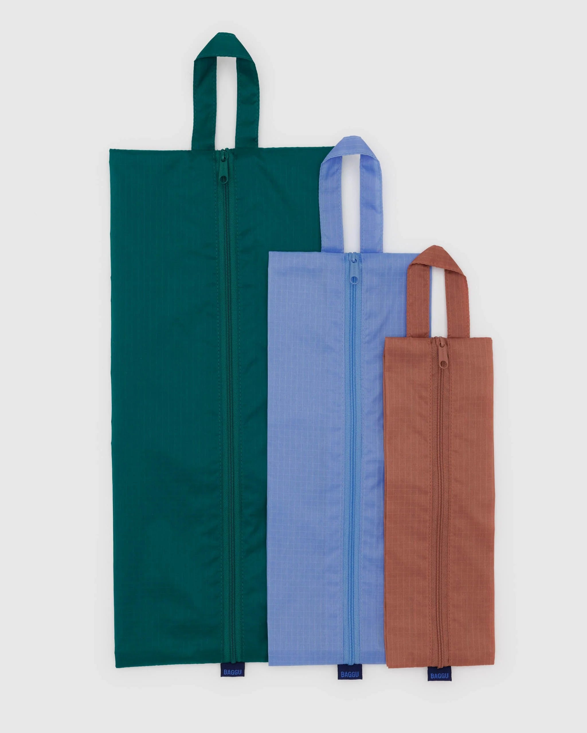 Das BAGGU 3D Zip Set von BAGGU besteht aus drei nachhaltigen Reißverschlusstaschen in Dunkelgrün, Hellblau und Braun, die jeweils einen Tragegriff haben - ideal für die Reiseorganisation.