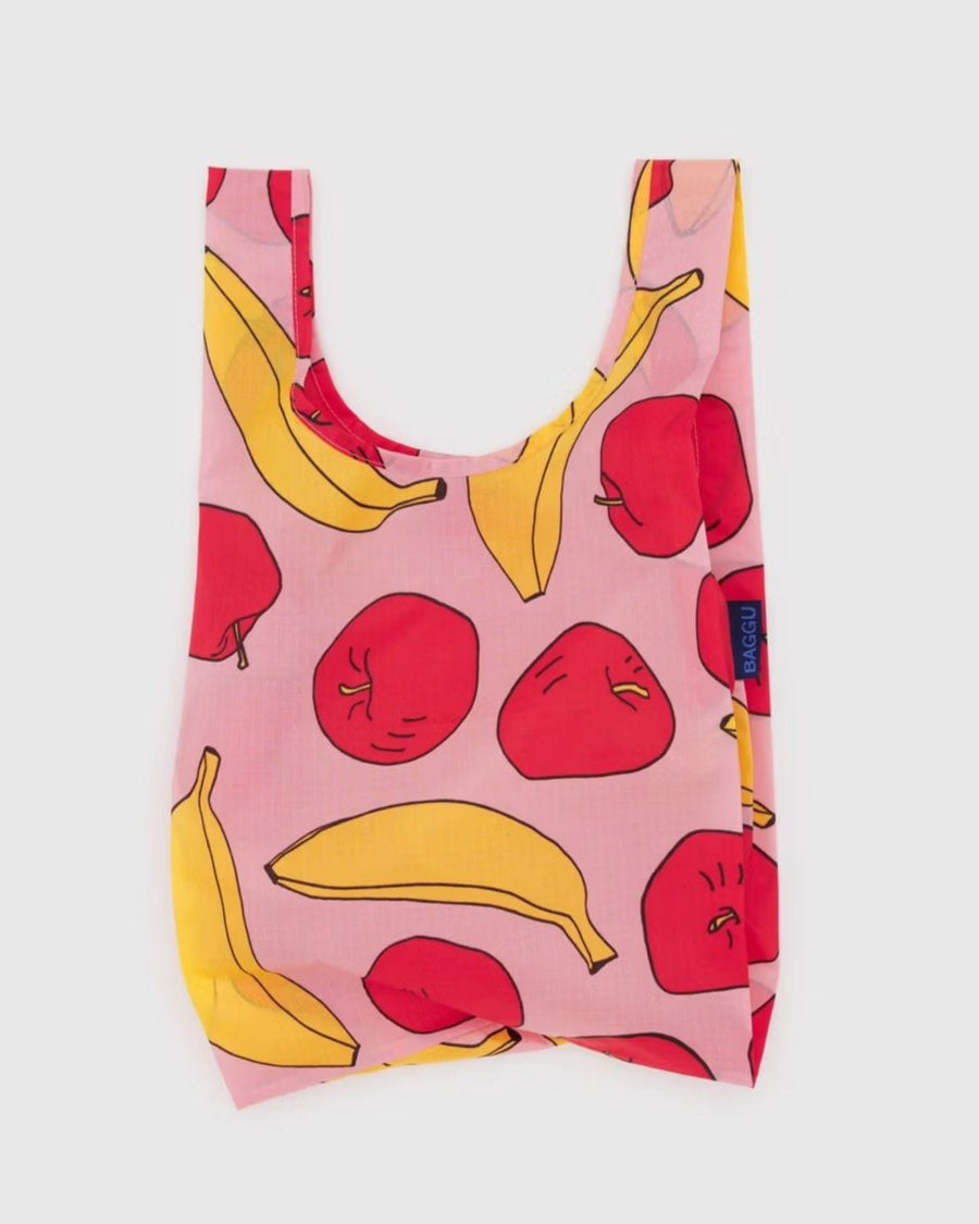 Die BAGGU Baby Tragetasche von BAGGU ist eine wiederverwendbare Tasche aus recyceltem Nylon mit einem rosa Hintergrund, der mit roten Äpfeln und gelben Bananen verziert ist. Sie hat breite Griffe, ein blaues Seitenetikett und ist perfekt für umweltfreundliches Einkaufen.