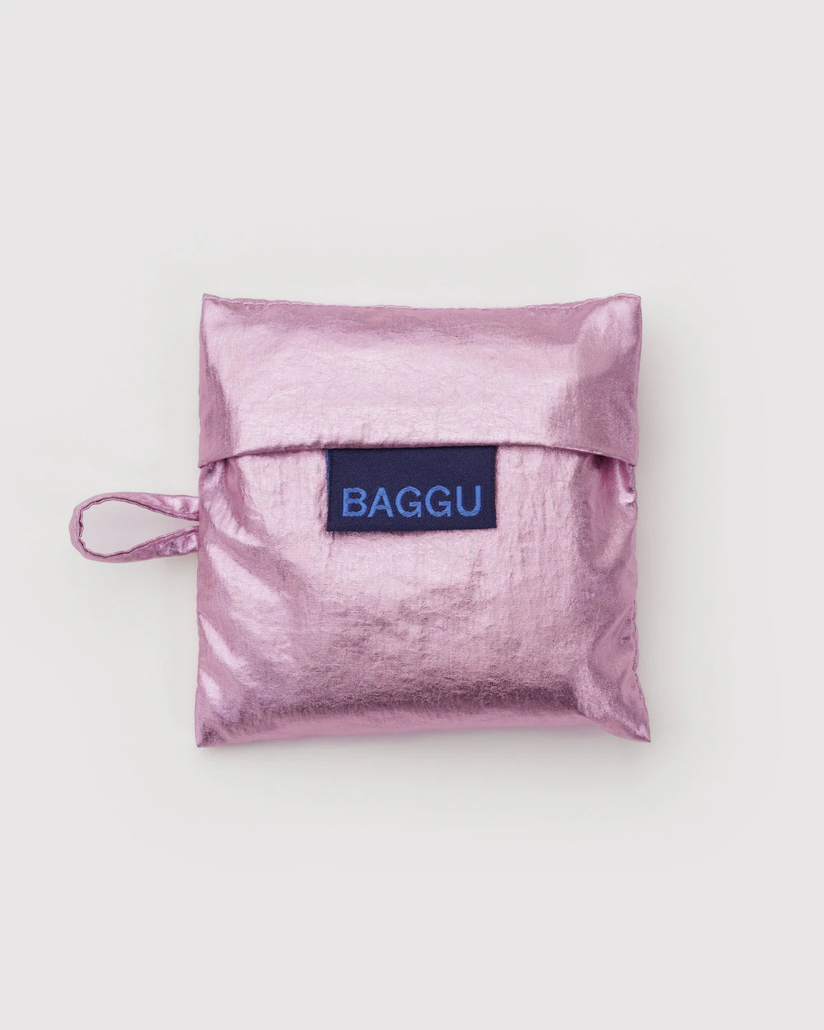 Die BAGGU Baby Tragetasche von BAGGU ist eine metallisch glänzende, pinkfarbene Tasche aus recyceltem Nylon mit einer Klappe, einer kleinen Seitenschlaufe und einem blauen "BAGGU"-Label auf der Vorderseite, das auf einem schlichten weißen Hintergrund abgebildet ist.