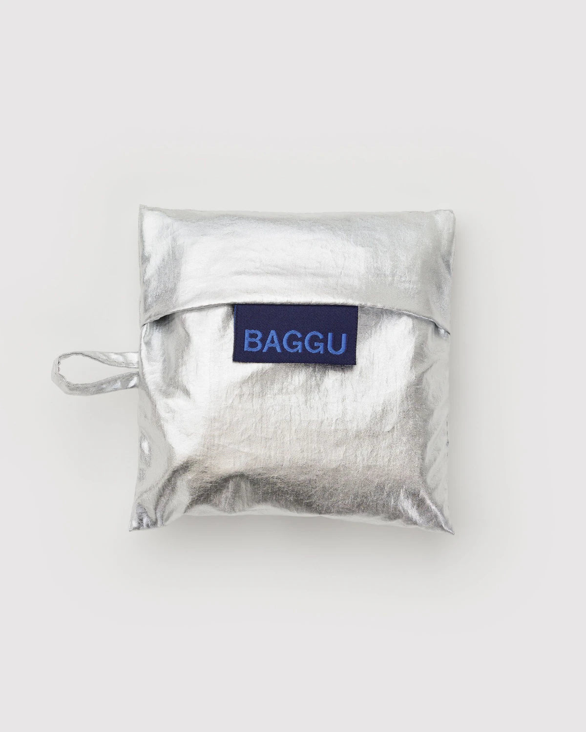 Die silbern glänzende BAGGU Baby Tragetasche von BAGGU besteht aus recyceltem Nylon, hat einen kleinen Henkel und eine Klappe mit "BAGGU" in Blau auf weißem Grund.