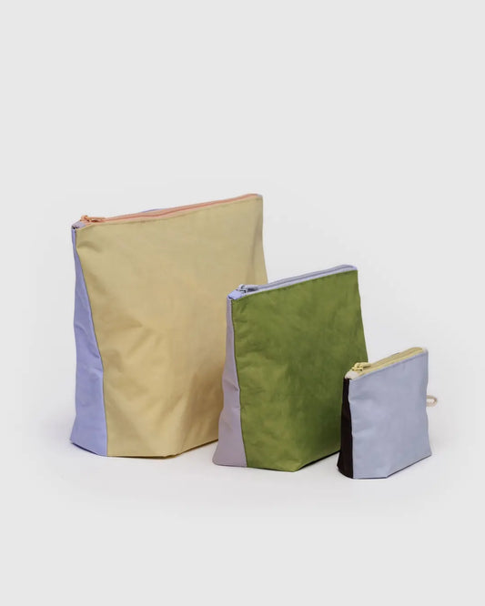 Das Main Design BAGGU Go Pouch Set umfasst drei Allzwecktaschen aus recyceltem Nylon: die größte ist gelb/blau, die mittlere ist grün/lila und die kleinste ist blau/braun. Jede hat eine rechteckige Form mit flacher Basis.