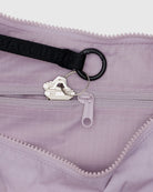 Nahaufnahme einer hellvioletten BAGGU Medium Nylon Crescent Bag von BAGGU mit einem schwarzen Schlüsselring, der zwei silberne Schlüssel hält und am inneren Riemen befestigt ist. Die Crossbody-Tasche verfügt über einen sichtbaren Reißverschluss und einen strapazierfähigen, strukturierten Stoff.